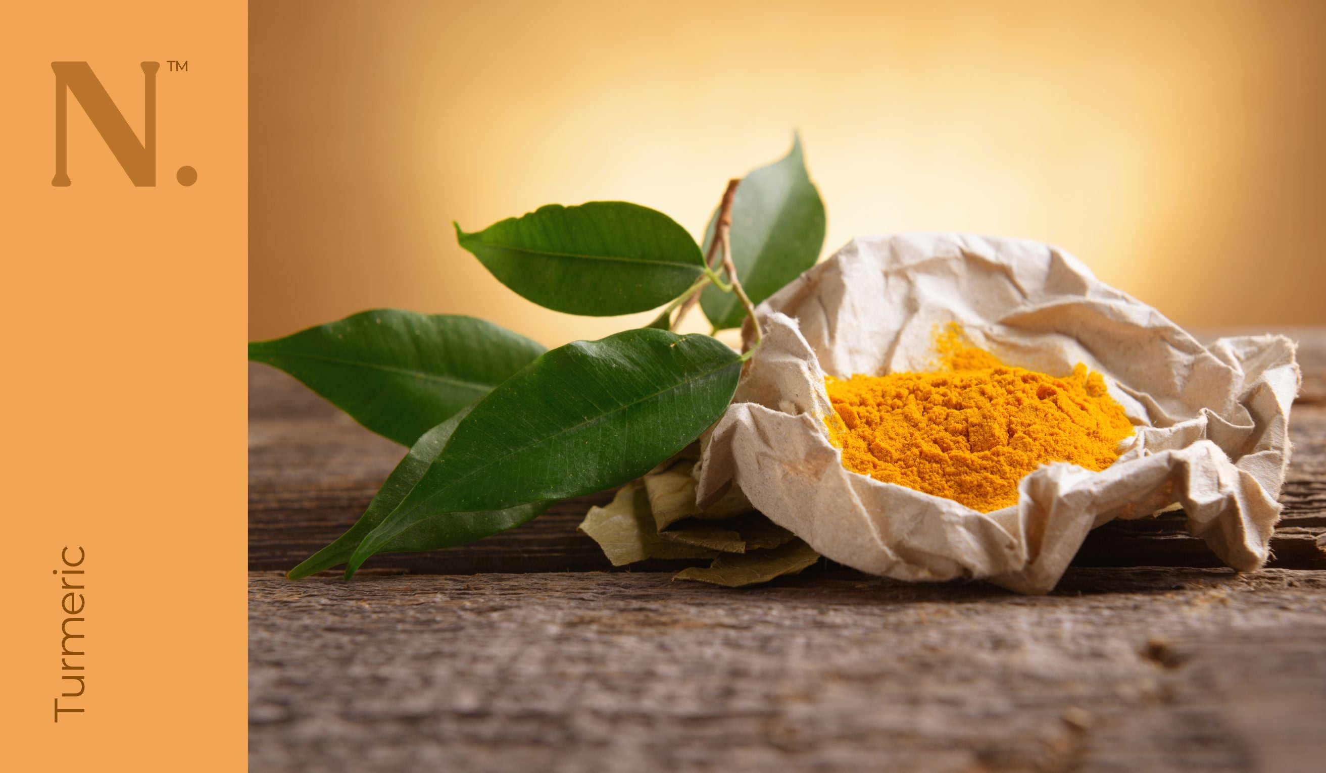 paper bowl with orange turmeric powder inside and leaves to the side of it on wooden surface - Turmeric