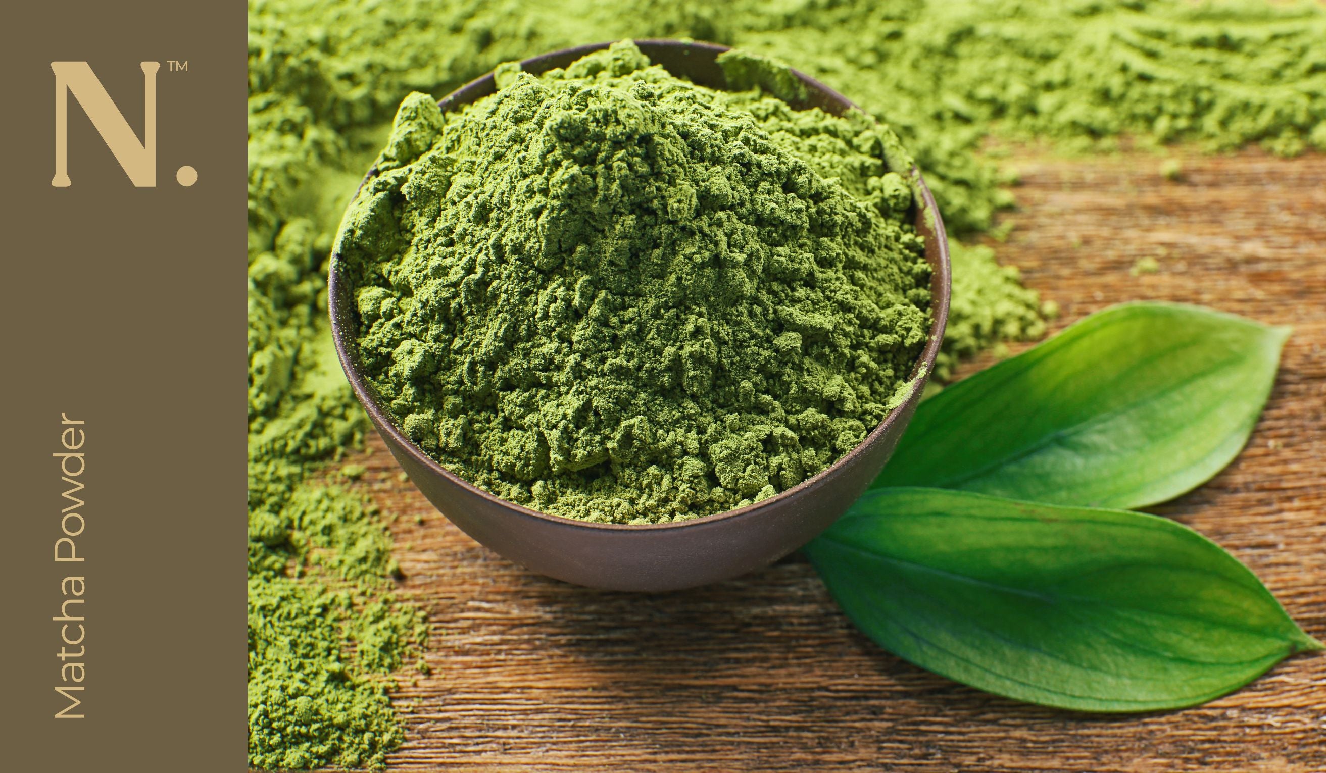 wooden bowl with green powder inside on wooden table with 2 leaves next to it - Matcha Powder