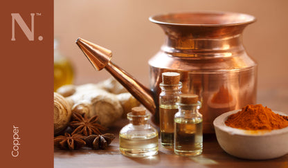 Copper teapot and glass bottles with cork lids, small bowl of orange powder and chunk of ginger on wooden surface - Copper